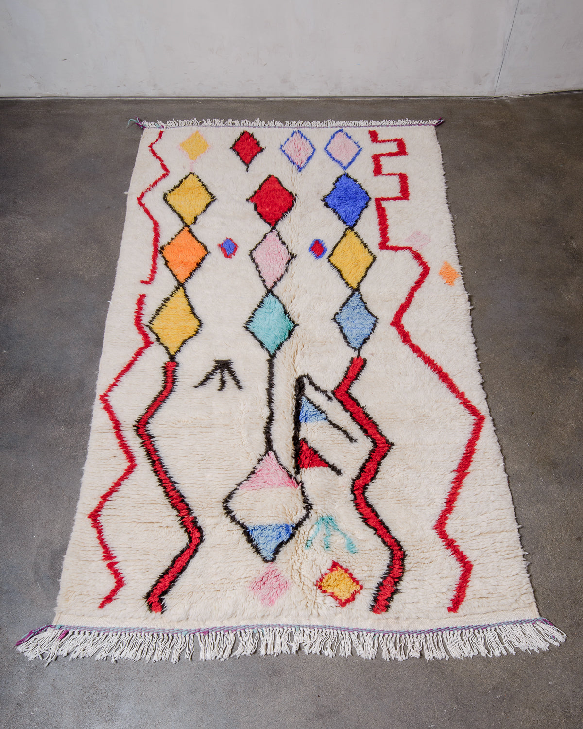 Berberlin Finest Rug made of plush cream wool with a colourful design, laying flat on concrete floor.